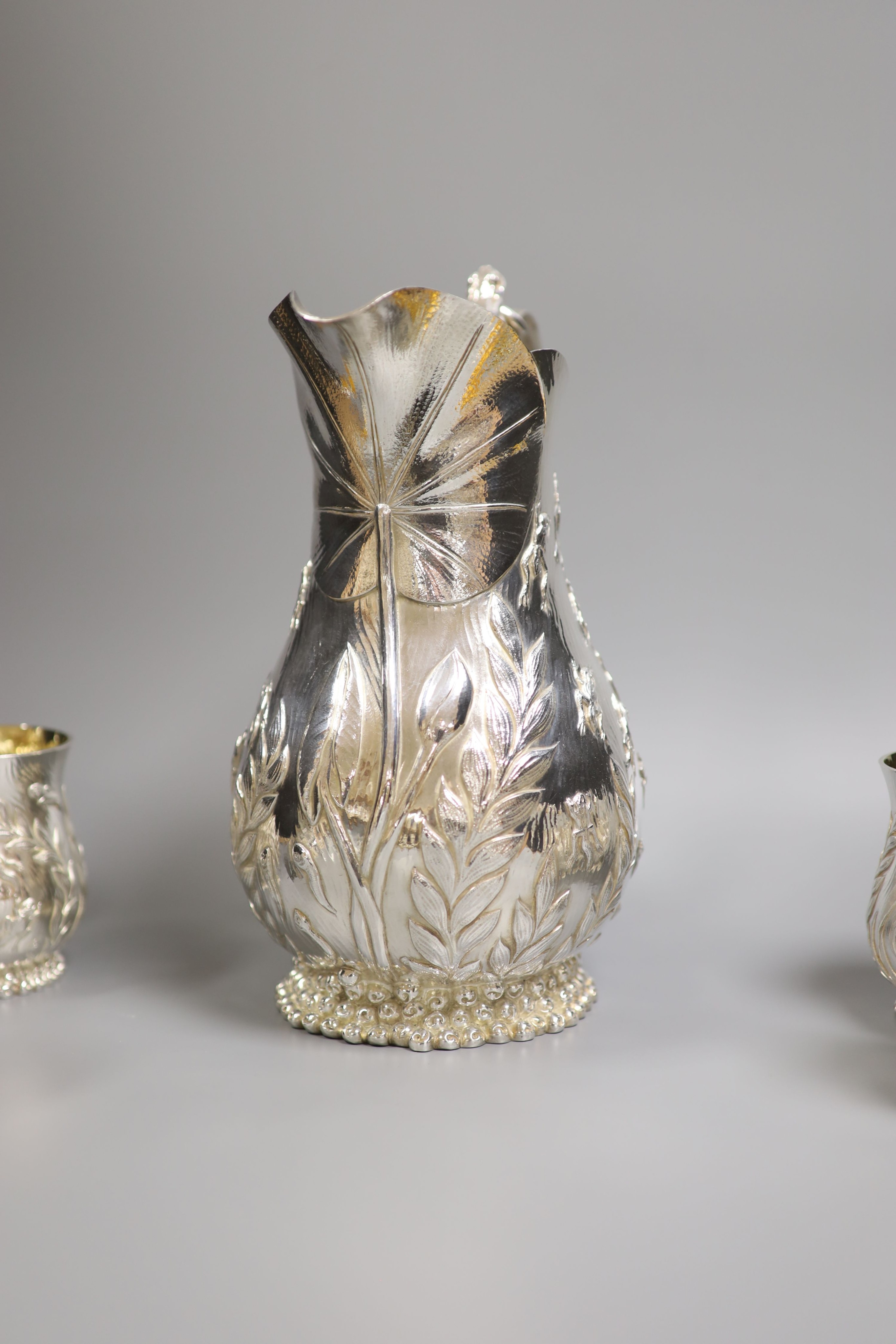 A good set of six Garrard & Co Ltd silver mugs and a matching jug, London, 1997, all embossed with frogs spawn amongst reeds, with gilded interiors, jug height 27.1cm